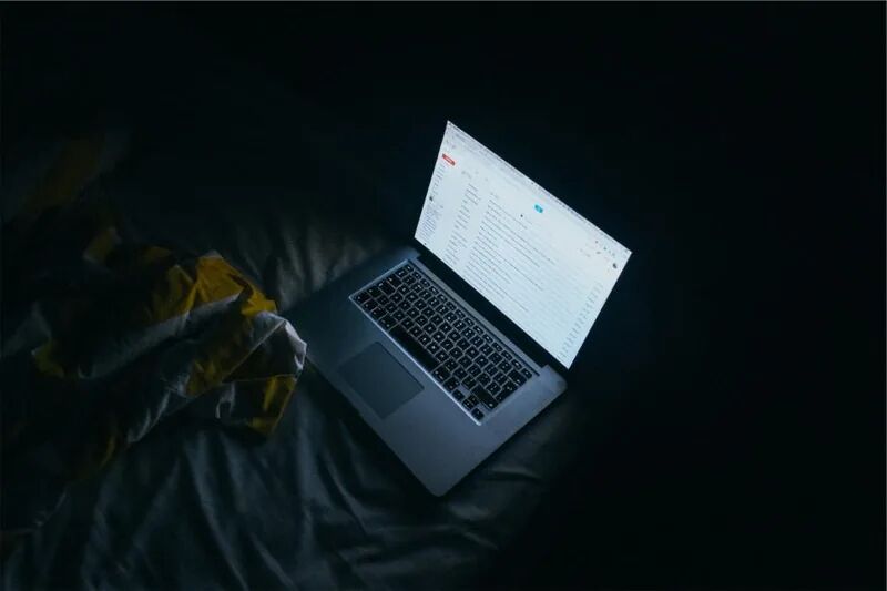 Laptop with an email inbox open in a dark room, representing invoice and wire fraud from business email compromise