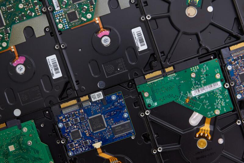 Several hard drives laid side by side face down, showing their green and blue circuit boards, representing data recovery after a hard drive failure