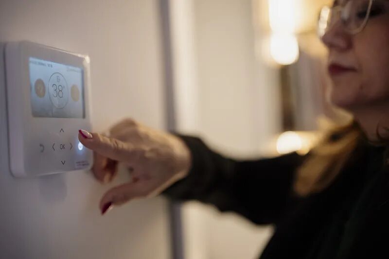 Homeowner adjusting a smart digital thermostat on a home wall to manage energy costs and cooling