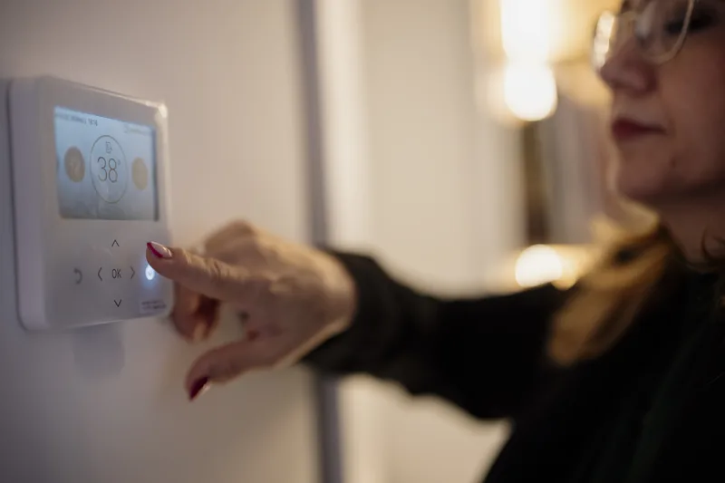 Homeowner adjusting a smart digital thermostat on a home wall to manage energy costs and cooling